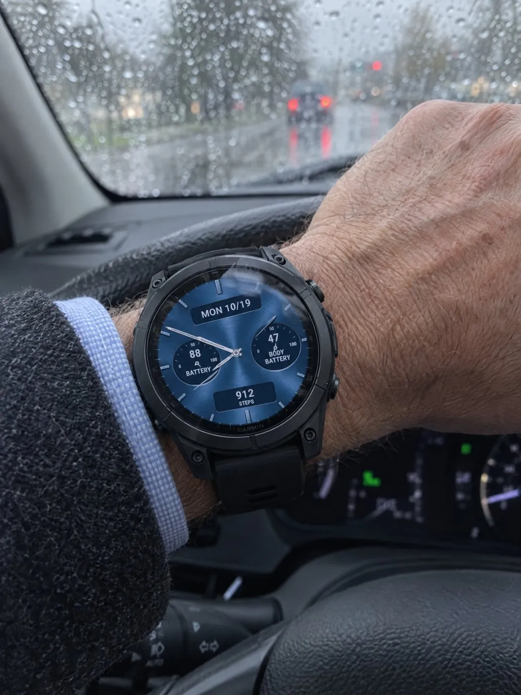 Classic Five Garmin watch face in blue on a fēnix E on a steering wheel in the rain