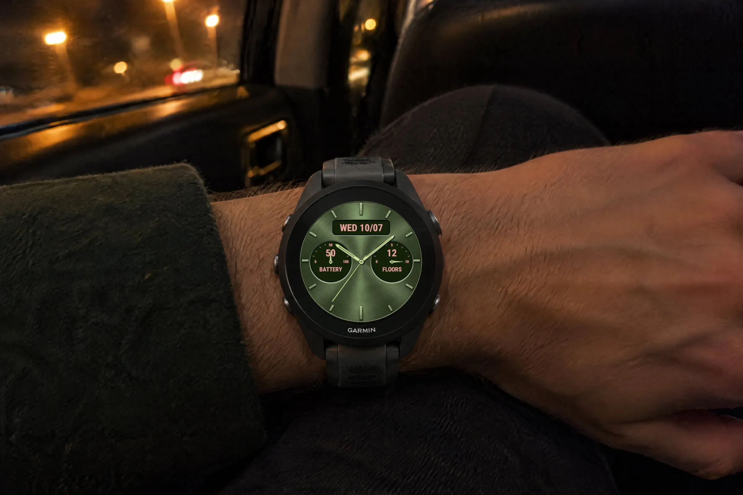 Garmin Forerunner 570 with the analog Classic Five watch face in green showing date, battery and floors in a taxi in the evening