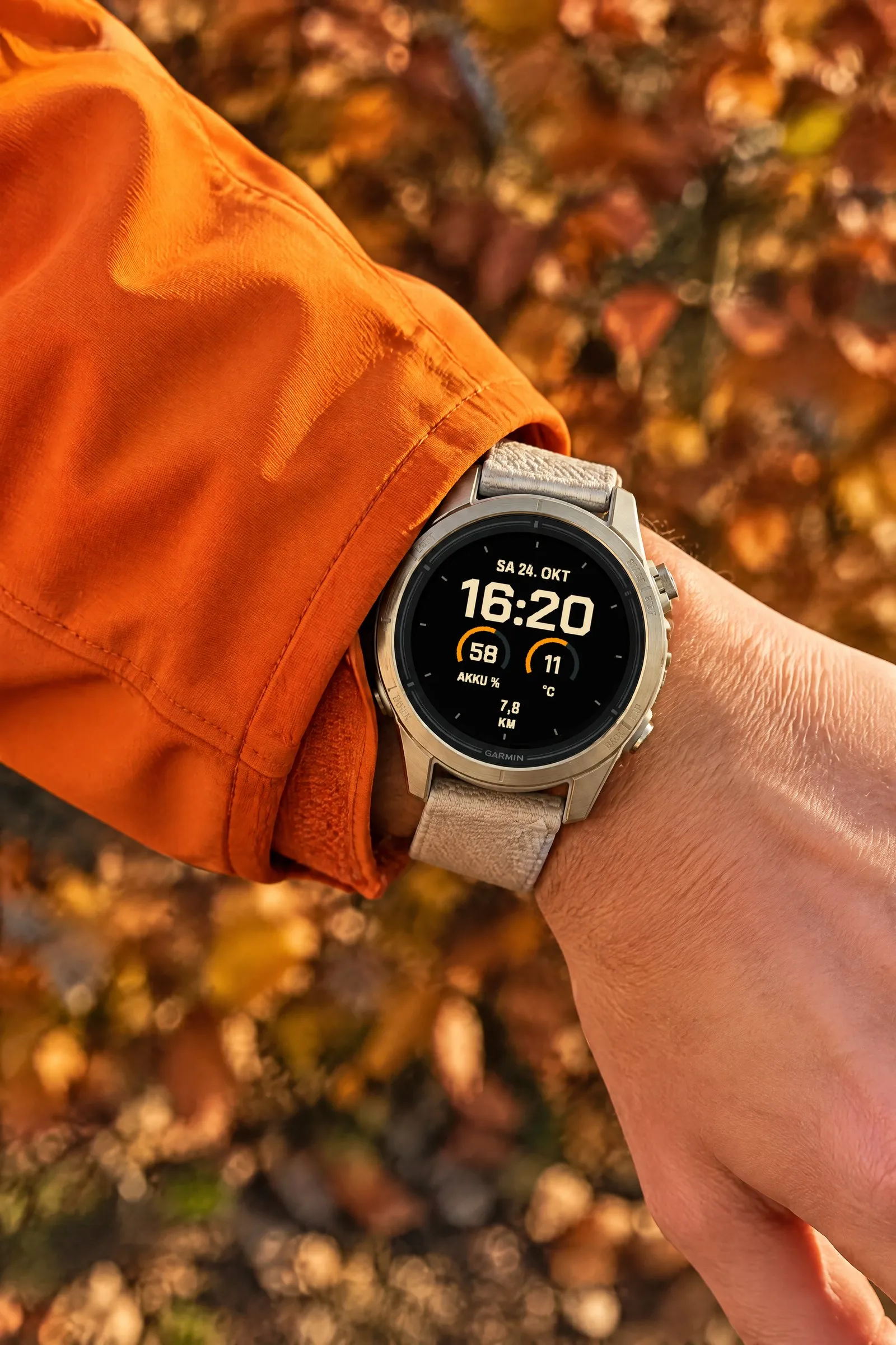 Garmin epix Pro mit dem Fieldline Watch Face in Creme / Orange und der Belegung Unterwegs am Ärmel einer orangefarbenen Jacke