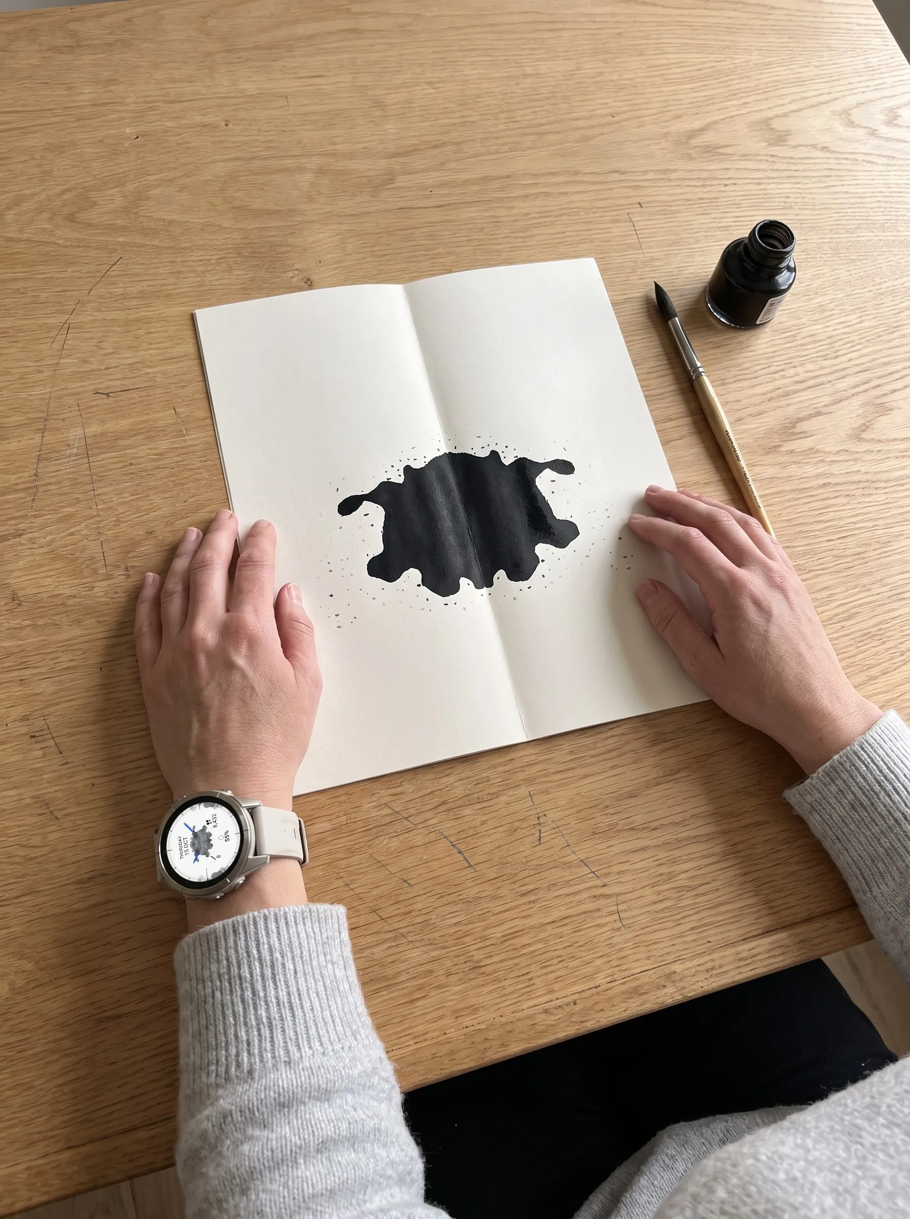 Hände falten ein Blatt mit frischem Tintenklecks, am Handgelenk eine fēnix 9 mit dem Garmin Watch Face Ulm