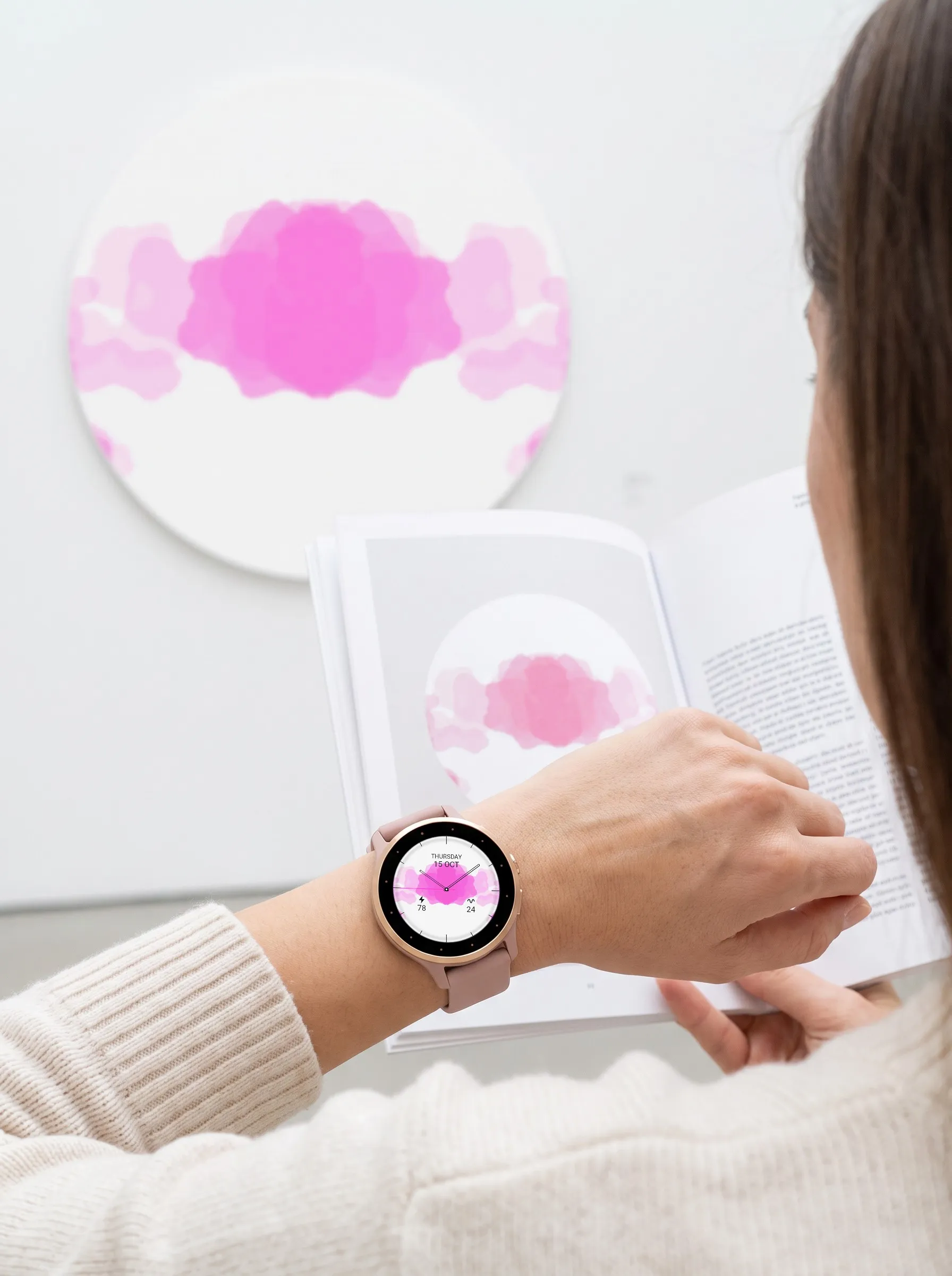 Analoges Garmin Watch Face Ulm mit pinkem Tintenklecks auf einer Venu 3S, Blick über die Schulter auf einen Ausstellungskatalog