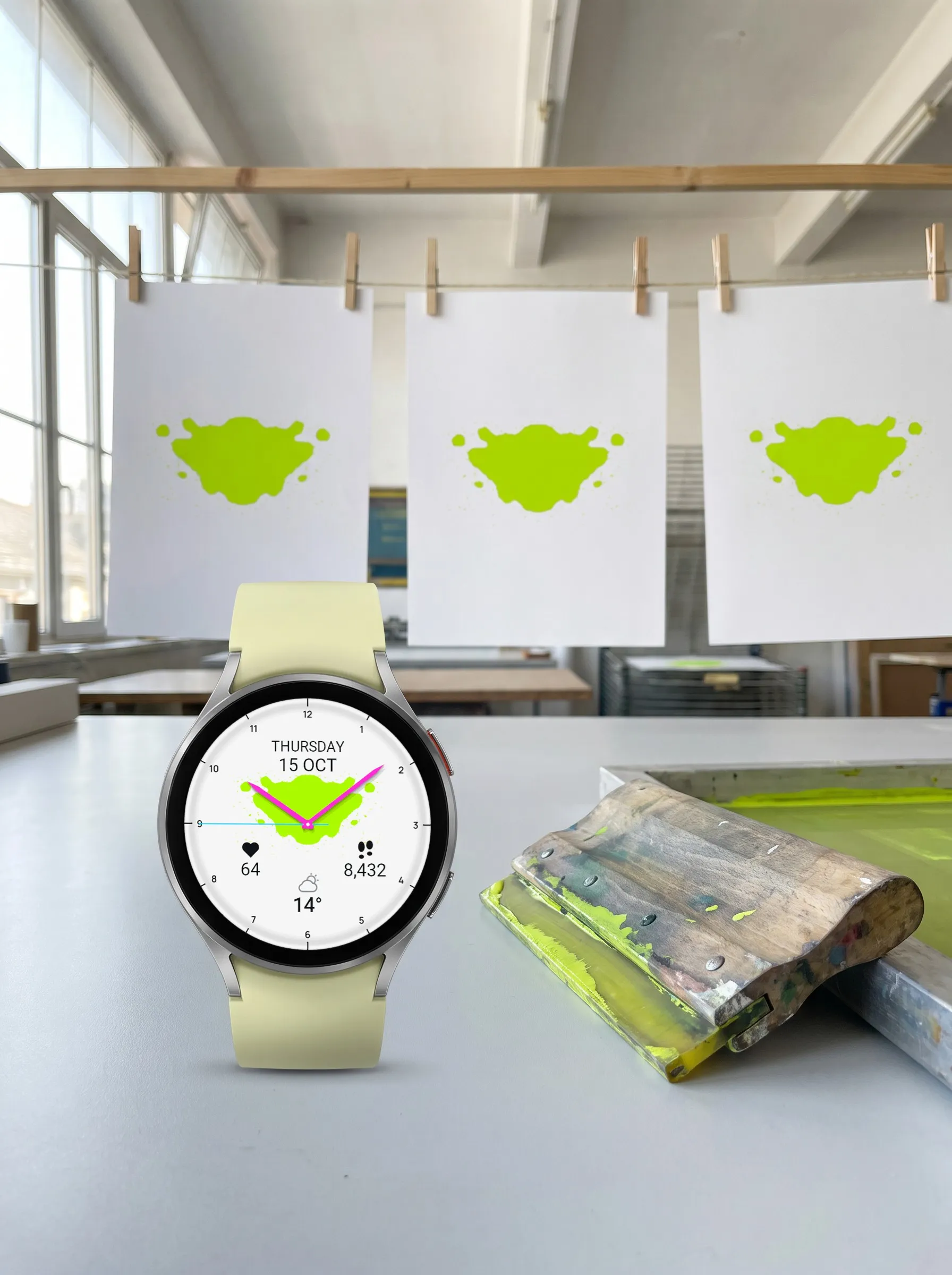 Garmin Venu 4 mit dem Watch Face Ulm in Limette in einer Siebdruckwerkstatt, dahinter drei Abzüge an der Leine