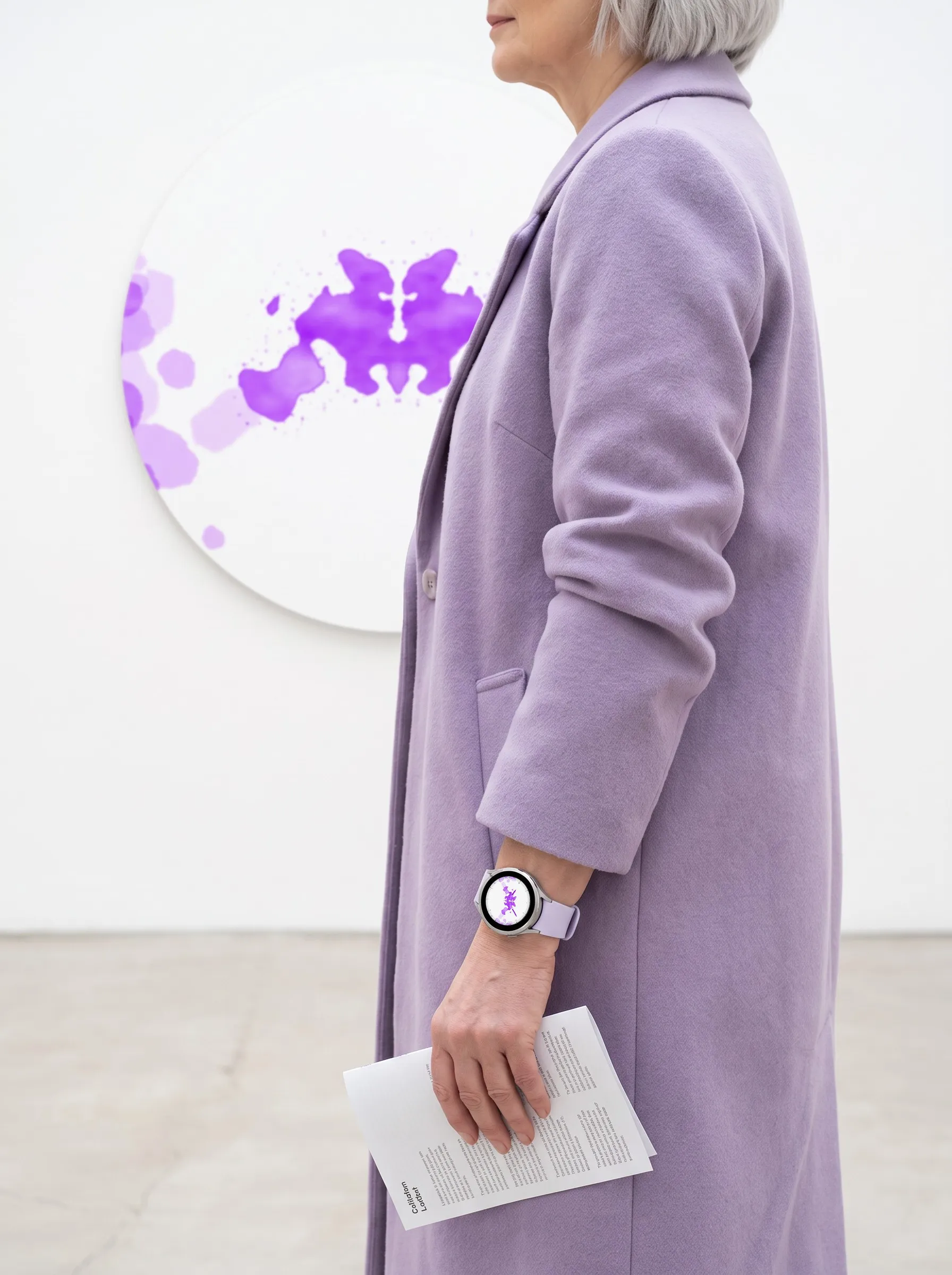 Frau im Mantel mit einer Venu 4 und dem Garmin Watch Face Ulm in Violett vor einer Tafel mit Tintenklecks