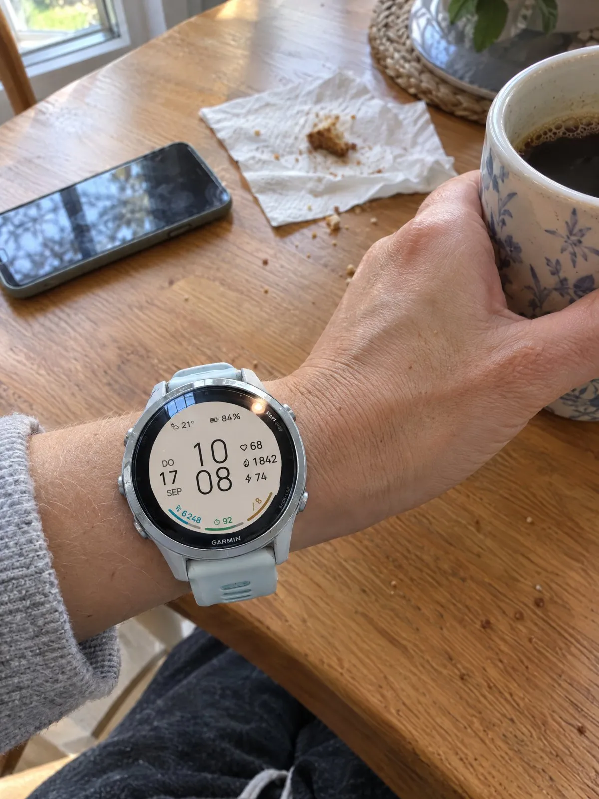 Garmin Forerunner 570 with the light ARCLINE watch face at the kitchen table, hand on a coffee mug